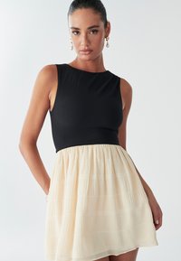 Zwarte mouwloze top met een textuurdesign, gecombineerd met een lichtgewicht crème rok met geplooide details en een uitlopende vorm.