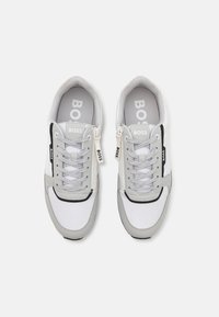 Harmaat ja valkoiset lenkkitossut, joissa on verkko- ja nahkamateriaaleja, nauhat ja sivuvetoketju. Brändäys näkyvissä kieliosassa ja sivulla.