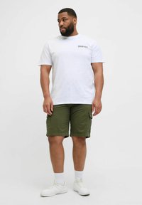 Camiseta blanca de algodón con un pequeño logo impreso, combinada con shorts de cargo verdes y zapatillas blancas con superficie texturizada y calcetines tobilleros.