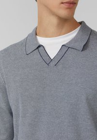 Koszulka polo w paski z dekoltem w kształcie litery V, wykonana z teksturowanej tkaniny z naprzemiennymi paskami w kolorach ciemnoniebieskim i jasnoniebieskim oraz kontrastującą białą warstwą wewnętrzną.