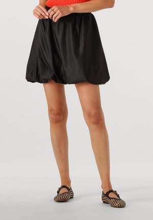 Zwarte satijnen pofrok met een elastische tailleband, met een gladde textuur en een ronde silhouet. Gecombineerd met geweven zwarte en tan schoenen.