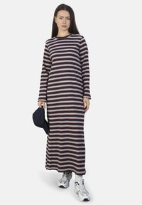 Gestreepte lange mouw jurk in navy, crème en bordeaux; katoenmix stof; losse pasvorm; ronde hals; model die een navy pet vasthoudt; gecombineerd met sneakers.