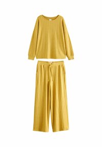 Žlutý loungewear set z hořčicové barvy obsahující žebrovaný dlouhý rukáv s kulatým výstřihem a kalhoty s širokými nohavicemi, elastickým pasem a kapsami.