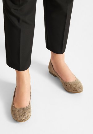 Beżowe baleriny z wyciętym kwiatowym wzorem, zaokrąglonym noskiem i niskim obcasem, zestawione z czarnymi spodniami o kroju 7/8.