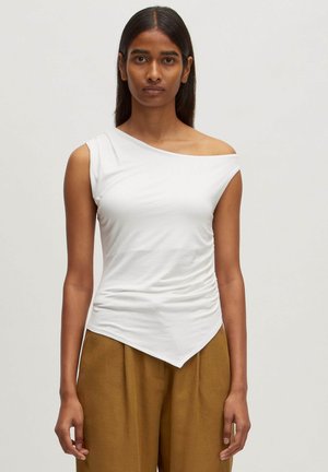 Asymmetrische witte gebreide top met een enkele schouderband, voorzien van geplooide textuur en een puntige zoom, gecombineerd met lichtbruine broeken.
