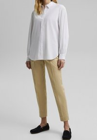 Camicia bianca a maniche lunghe con colletto classico, abbinata a pantaloni beige slim-fit e mocassini neri. Tessuto liscio, vestibilità rilassata.