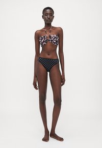 Haut de bikini floral avec un détail de nœud et des bretelles halter ; associé à un bas taille haute en noir à pois. Tissu lisse, design ajusté.
