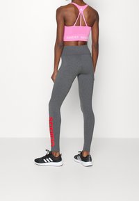 Grå leggings med en tight design, röd "adidas"-logga längs sidan, tillsammans med en rosa sport-bh med racerback-design.