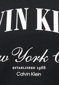 Μαύρο ύφασμα με λευκό κείμενο που γράφει "Calvin Klein New York City Established 1968" σε διάφορες γραμματοσειρές.