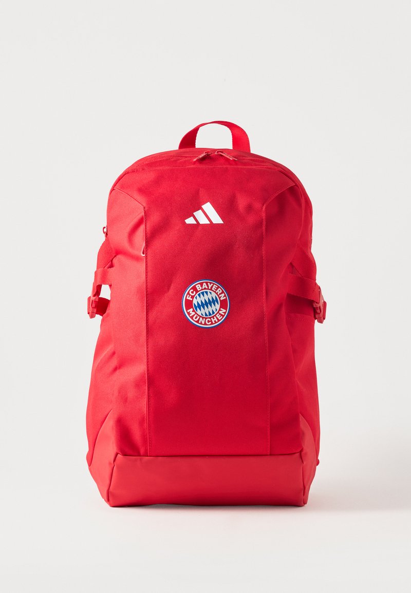 Κόκκινο σακίδιο με το λογότυπο της FC Bayern Munich και λευκό έμβλημα Adidas, εμπρός φερμουάρ, πλαϊνές λουρίδες και κορυφαία λαβή μεταφοράς σε λευκό φόντο.