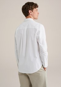 Witte button-up shirt met lange mouwen, voorzien van een klassieke kraag, een rugplooi en een afgeronde onderrand, gecombineerd met lichtbeige broek.