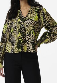 Blouse à motif léopard avec des accents verts et noirs vibrants, décolleté en V, manches retroussées et coupe décontractée, confectionnée dans un tissu léger.