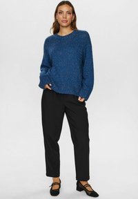 Trikotēts zils džemperis ar teksturētu rakstu, noapaļotu kakla izgriezumu un brīvu piegriezumu. Saskaņots ar pielāgotām melnām biksēm un melnām kurpēm.