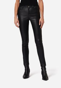 Svarta läder skinny byxor med en slät yta, femficksdesign och metallknappstängning. Matchas med svarta klackade ankelstövlar.