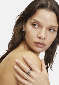 Zilveren ring met een gelaagd ontwerp, met gepolijste en gestructureerde oppervlakken. De hand van het model rust op de schouder en toont de details van de ring.