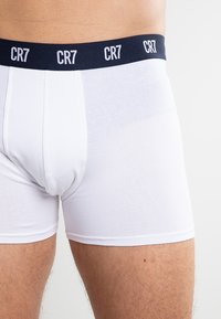 White cotton boxer shorts with a navy elastic waistband featuring white "CR7" branding. Smooth texture, fitted cut, and mid-thigh length.