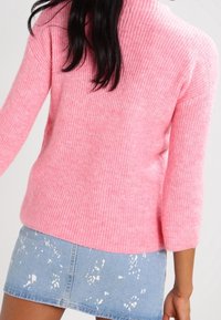 Rosa gerippter Pullover mit hohem Kragen und langen Ärmeln, kombiniert mit einem hellen Denim-Rock mit Spritzmuster.
