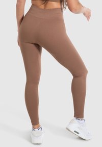 Leggings marroni a costine con un'alta vita, design aderente e texture morbida, abbinati a sneakers bianche con accenti neri.
