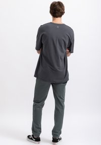 Donkergrijze t-shirt met korte mouwen en een ronde zoom, met een logodetail op de rug, gecombineerd met groene afgebouwde broek en zwarte sneakers.