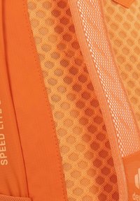 Sezione di uno zaino arancione con texture a rete a nido d'ape e tessuto liscio, con accenti bianchi e etichettatura del marchio sul lato.