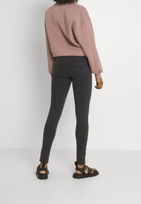Jeans skinny grises de cintura alta, con bolsillos traseros. Combinados con un sudadera rosa y sandalias negras de tiras.