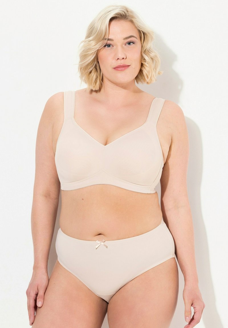 Soutien-gorge beige avec de larges bretelles et une finition lisse, présentant un design structuré et des coutures discrètes. Assorti à une culotte taille haute.