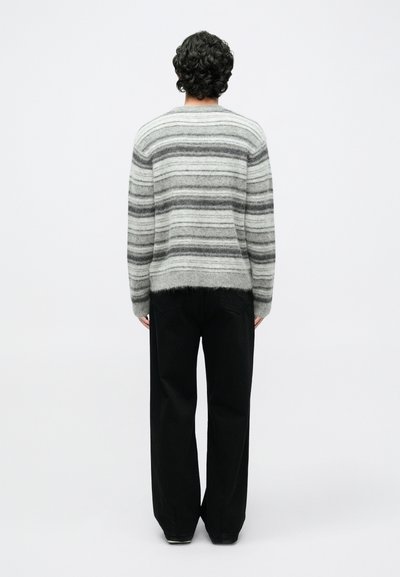 Sivi i crni prugasti vuneni džemper s okruglim izrezom, s blago skraćenim rubom i opuštenim krojem, upareni s crnim hlačama širokih nogavica.