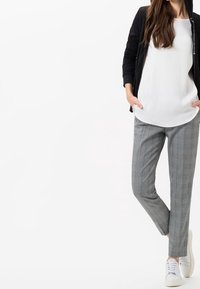 White top with a loose fit, black zip-up jacket, gray plaid slim-fit pants, and white sneakers. The outfit features a minimalist design.