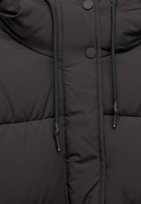 Veste matelassée noire en gros plan présentant un tissu lisse, un col courbé, des boutons-pression noirs et des cordons de serrage ajustables pour un ajustement parfait.