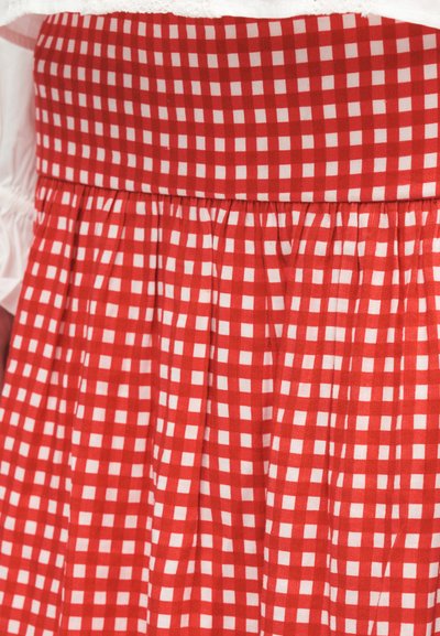 Φόρεμα με κόκκινο και λευκό καρό μοτίβο gingham και σφηκωμένη μέση, φορεμένο πάνω από λευκό ρούχο με μακριά μανίκια.