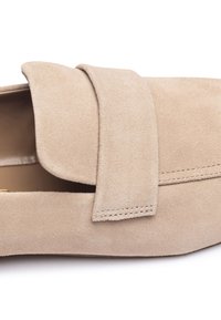 Beige suède loafers met een gevouwen bovenste riem, een gladde textuur en zichtbare stiksels langs de rand, ontworpen voor comfort en stijl.