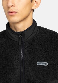 Giacca in pile nera con colletto alto, chiusura con zip e tessuto testurizzato. Presenta un patch con il logo "element" sul petto.