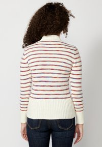 Maglione a righe con collo alto, caratterizzato da righe sottili alternate rosse, blu e gialle su una base crema; orlo e polsini a coste.