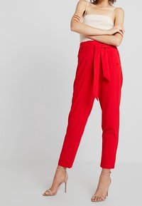 Pantalons ajustés rouges avec une taille large et un détail de ceinture nouée, présentant une silhouette épurée et une longueur à la cheville.