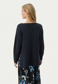 Pull à manches longues bleu marine foncé avec un col rond et une coupe décontractée, présentant une texture douce et un léger design à épaule tombante.