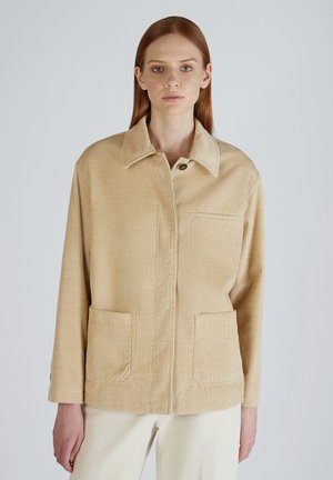 Beige corduroy jas met een kraag, sluiting met knopen aan de voorkant, twee voorzakken en een getextureerd ribbelpatroon.