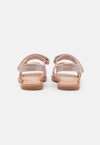 Rosa vevde sandaler har flate såler, to justerbare stropper og en glatt overflate. Hælen er åpen, med en naturlig fargebunn.