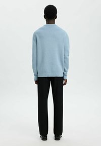 Svijetloplava pletena puloverica s okruglim izrezom, rebrastim manžetama i rubom, u kombinaciji s crnim hlačama i crnim cipelama. Pogled straga.