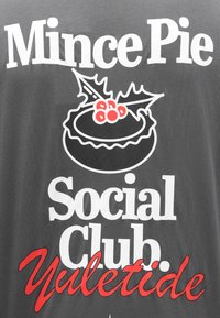Šedá textília s výrazným bielym a červeným textom: "Mince Pie Social Club Yuletide" s dekoratívnou čiernou grafikou koláča a cesmíny.
