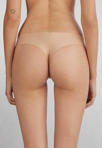 Beige sömlösa underkläder med en mjuk textur, minimal täckning och en låg midjeband. Hudfärgen smälter in med kroppen.