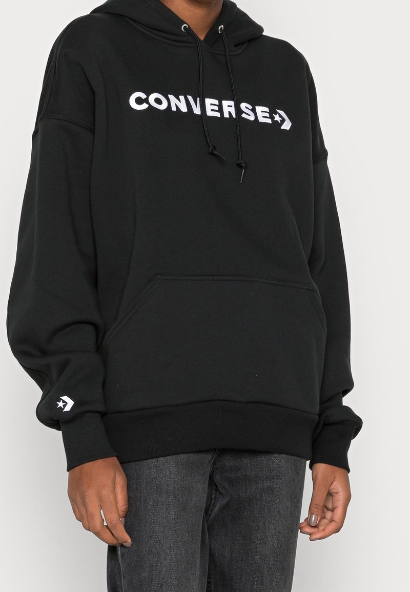 Felpa con cappuccio nera in morbido tessuto, caratterizzata da un grande logo bianco "CONVERSE" sul petto e il logo della stella sulla manica.