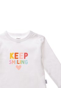 Weißes langärmliges Hemd mit buntem Aufdruck, der "KEEP SMILING" und ein kleines Herz zeigt. Hergestellt aus weicher Stoffqualität mit Druckknopfverschluss.
