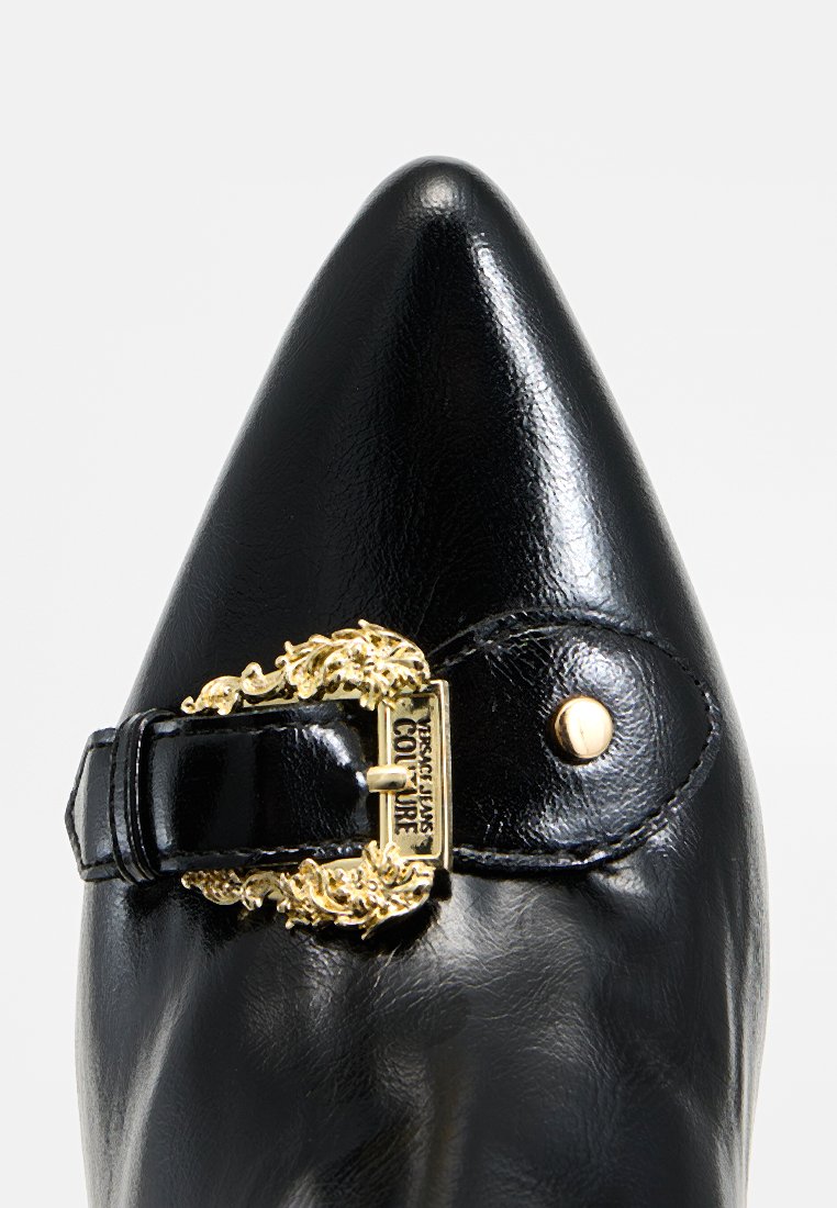 Czarna, spiczasta skórzana szpilka z złotą ozdobną klamrą i paskiem na górze, przeszyta małym złotym nitką.