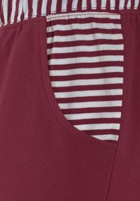 Burgundy pants with a striped pocket. Soft cotton material, elastic waistband, and contrasting white and burgundy stripes on the pocket.