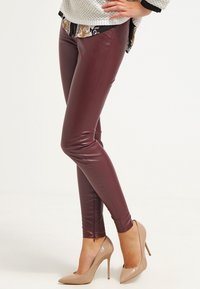 Burgundowe legginsy z sztucznej skóry o dopasowanym kroju, z gładką fakturą i zamkami błyskawicznymi przy kostkach, zestawione z cielistymi szpilkami.