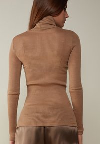 Zgniła bluzka z golfem w ciepłym beżu. Ma długie rękawy i dopasowany krój. Miękka tekstura z pionowymi paskami dla dodatkowego szczegółu.