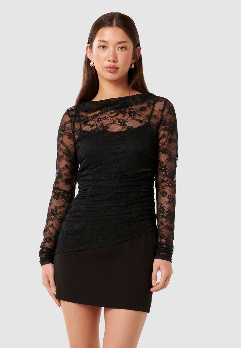 Μαύρο φόρεμα με μακριά δαντελένια μανίκια, προυσαρισμένο μπούστο, εφαρμοστή σιλουέτα και αέρινο τμήμα φούστας, δημιουργώντας αντίθεση σε υφή με στρώματα.