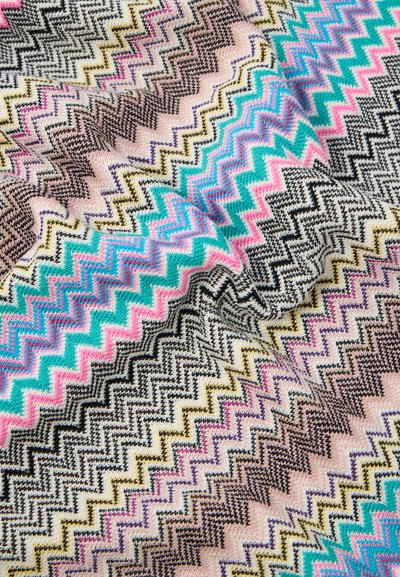 Close-up van een textuurstof met een kleurrijk zigzagpatroon in roze, turquoise, zwart, geel en crème tinten.