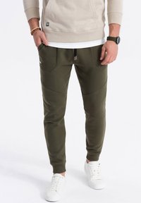 Olijfgroene joggerbroeken hebben een taps toelopend ontwerp, een elastische tailleband met trekkoord en twee voorzakken. Gemaakt van zachte stof.