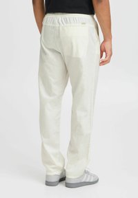 Lyse beige, løst siddende bukser med elastisk talje, sidelommer og en struktureret stof. Båret med grå sneakers.
